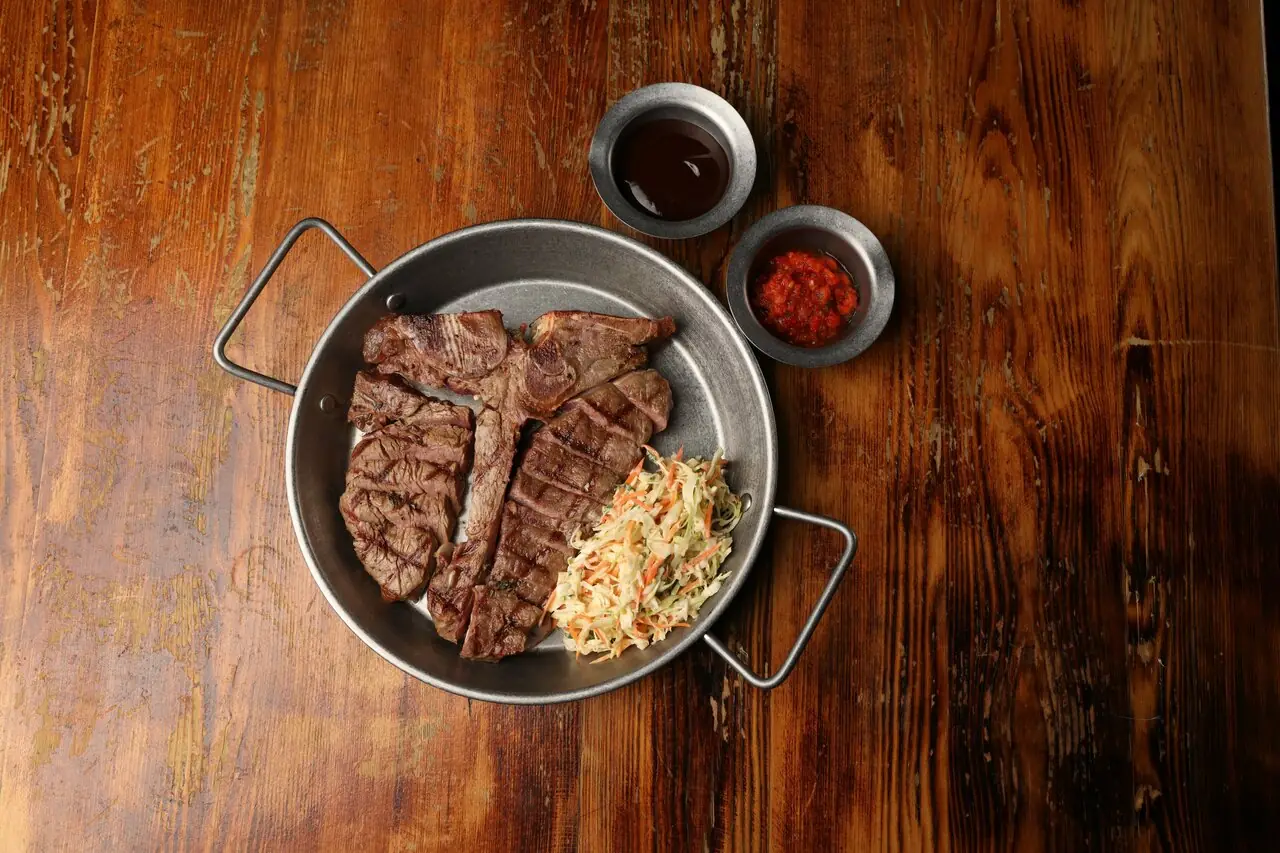 T-bone на стальной сковороде с соусами на тёмном столе